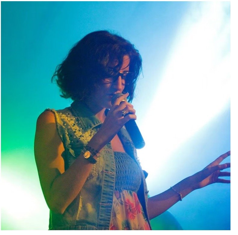 Donna che canta dal vivo con microfono in mano sotto luci da concerto.