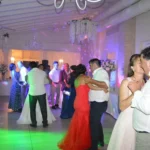 Coppia che posa sorridente per una foto tra gli ospiti durante una festa di matrimonio.