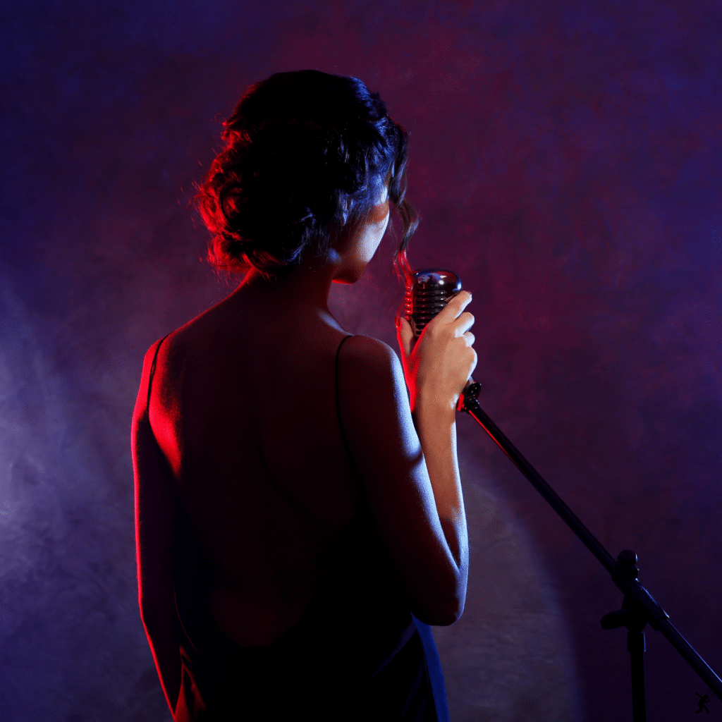 Cantante con microfono vintage sul palco, illuminata da luci sceniche rosse e blu.