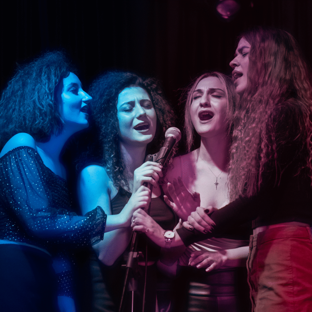 Gruppo di quattro cantanti che eseguono una performance dal vivo con luci blu e rosa sul palco.