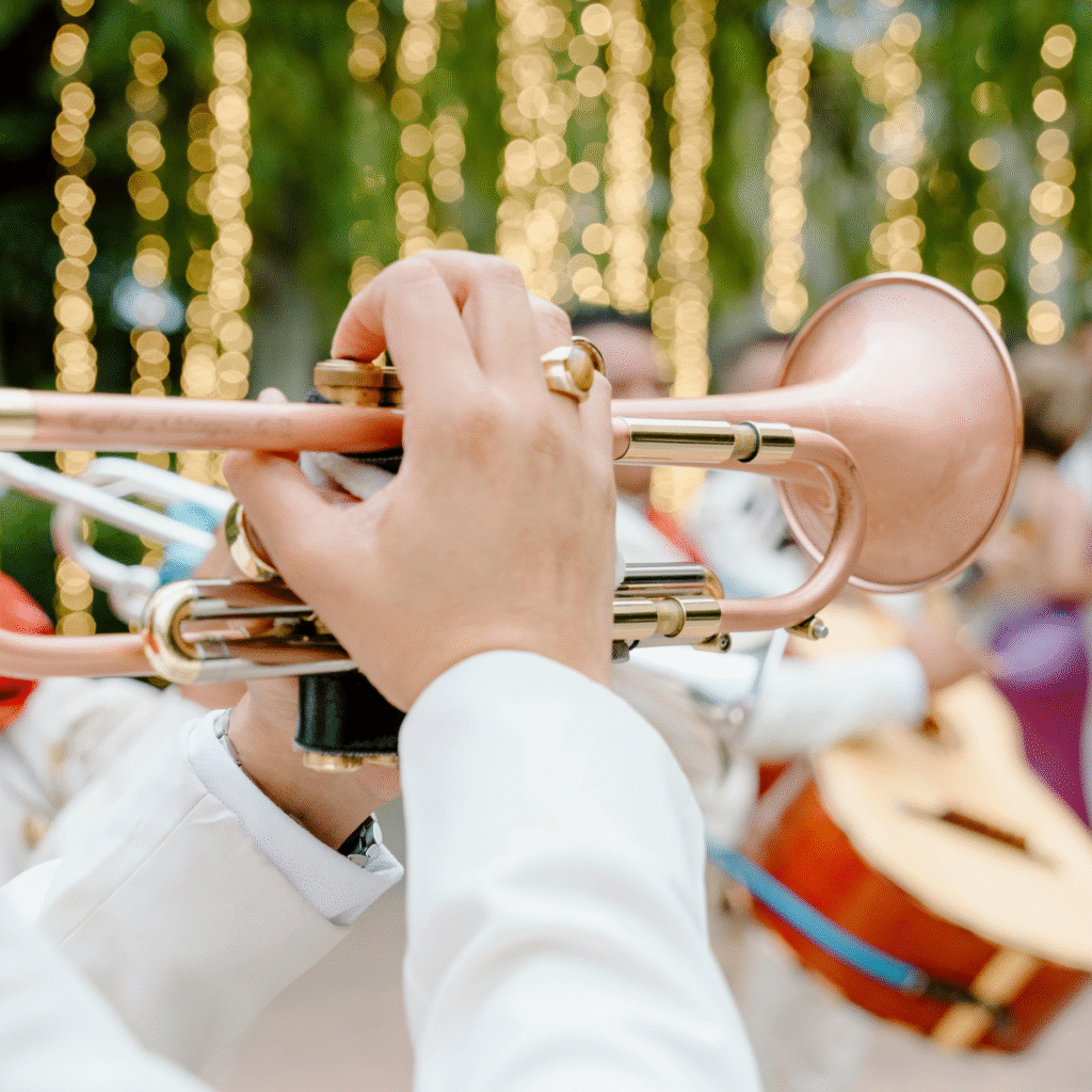 Musicista che suona la tromba con luci decorative sullo sfondo in un evento all’aperto.