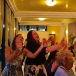 Due donne cantano sorridenti durante il ricevimento con musica dal vivo e ospiti festosi.